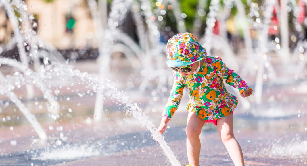 Una niña con gafas de sol y gorro para protegerse del sol juega con chorros de agua de una fuente pública aviso amarillo ola de calor alava vitoria foto de depositphotos