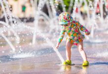 Una niña con gafas de sol y gorro para protegerse del sol juega con chorros de agua de una fuente pública aviso amarillo ola de calor alava vitoria foto de depositphotos