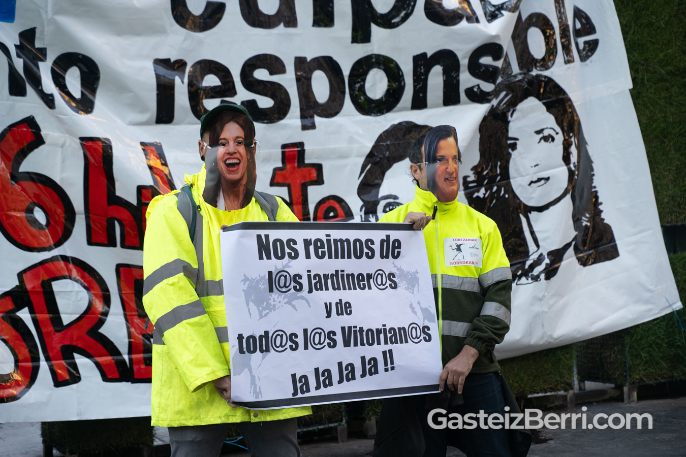 Dos personas con caretas de Maider Etxebarria, alcaldesa, y Beatriz Artolazabal, teniente de alcaldesa con una pancarta que dice "Nos reímos de l@s jardiner@s y de todos y todas l@s Vitorian@s Ja Ja Ja Ja !!"